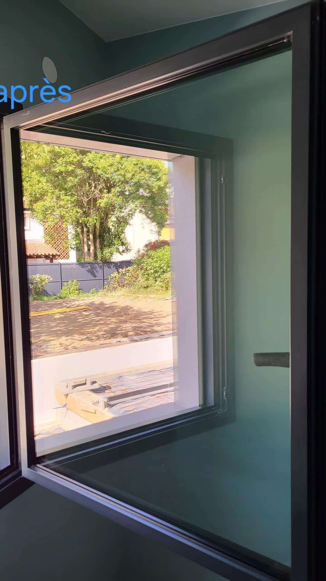 Nouvelle baie vitrée noire ouverte, vue sur un jardin avec clôture. Mur intérieur bleu-vert. Texte 'après' visible. Installation récente.