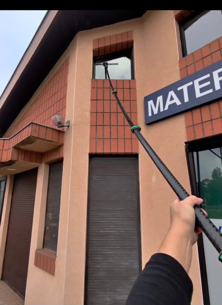 Nettoyage de vitre haute : perche télescopique professionnelle utilisée sur une façade commerciale beige et brique, près de l'enseigne "MATEF".